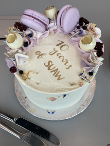 a tall cake covered in purple macrons and icing, reading in gold lettering 10 years of SUAW